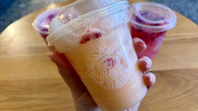 A hand holding a Starbucks Mango Dream Drink with other drinks in the background