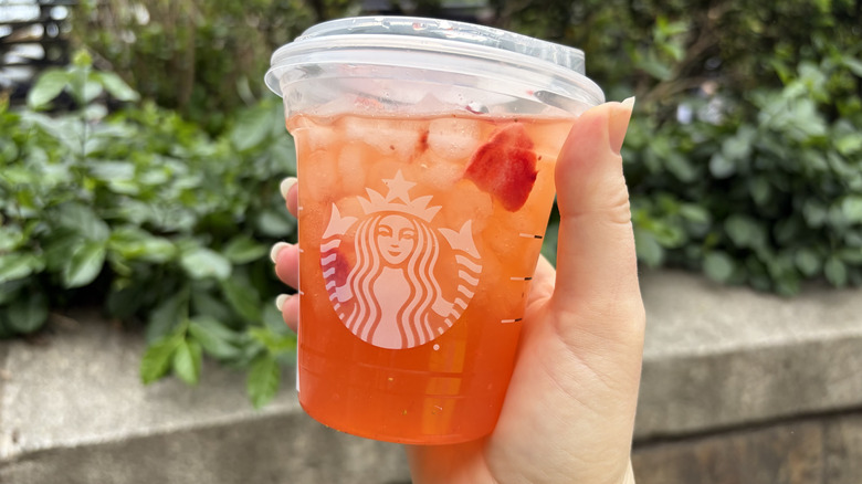 A hand holding a Starbucks Mango Strawberry Lemonade Refresher