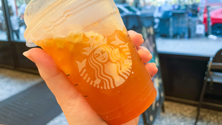 Hand holding the Spicy Pineapple Refresher in front of a Starbucks window