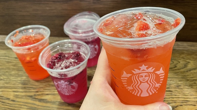 Hand holding the Strawberry Açaí Lemonade Refresher over other drinks on a table