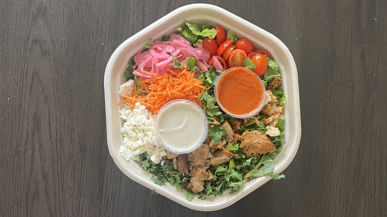 Sweetgreen buffalo chicken salad in to-go container with two dressing inside the salad in separate containers