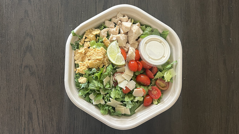 Sweetgreen kale Caesar salad in to-go container with salads, chicken, tomatoes, dressing, and a lime wedge