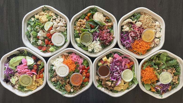 Top view of seven different Sweetgreen salads in to-go container