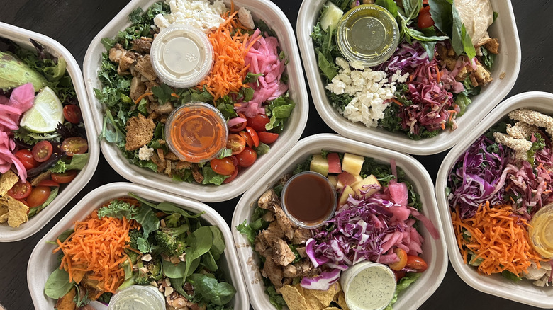 Top view of seven different Sweetgreen salads in to-go container