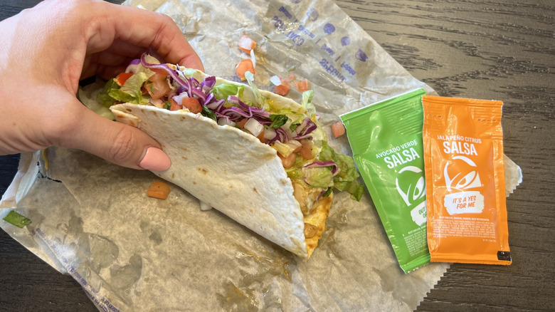 Hand holding Taco Bell Cantina Chicken soft taco with sauce packets.