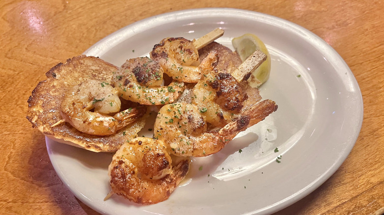 Six pieces of shrimp with a bread roll on a plate
