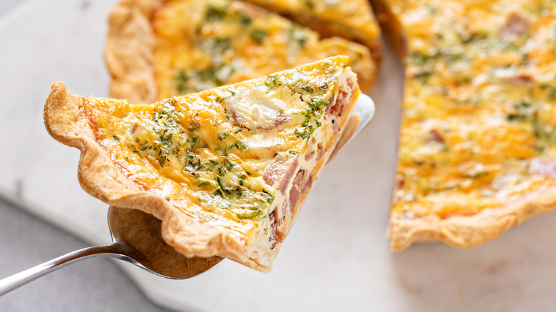 Slice of quiche with ham and herbs being picked up with a pie server