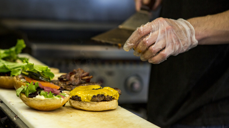 a chef putting multiple toppings on a burger