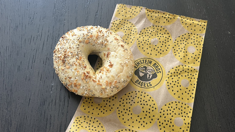 Einstein Bros. Bagels everything bagel on a to-go bag laid out on a dark wooden surface