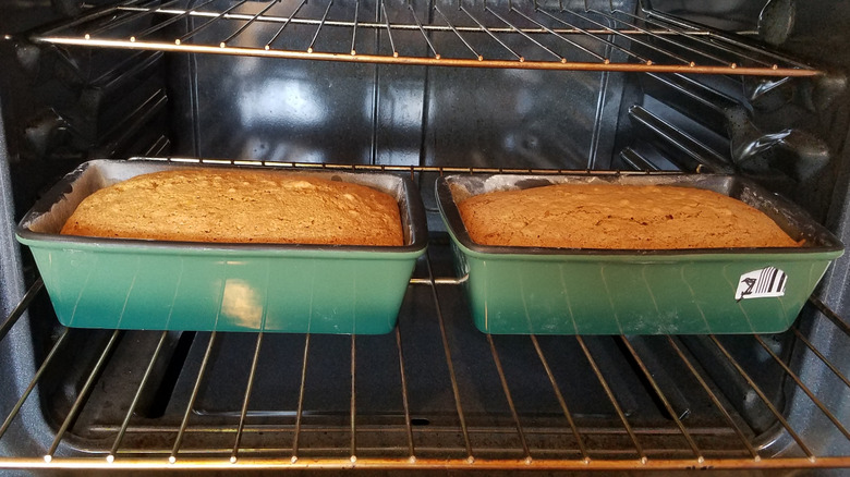 two loaves of quick bread, in matching green-enameled loaf pans, ready to come out of the opened oven