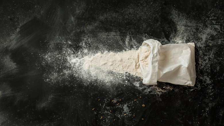 unidentified flour spilling out of an unmarked bag, on a black surfaced countertop