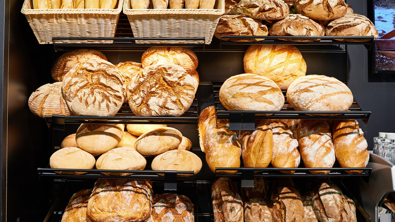 bakery display with multiple kinds of artisan bread on racks, and baskets of baguettes just visible at the top