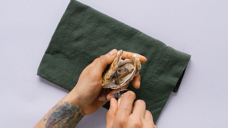 Top-down shot of hands lifting the lid off of oyster on green napkin