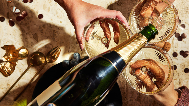 Aerial view of a bottle of champagne pouring into wide coupe glasses