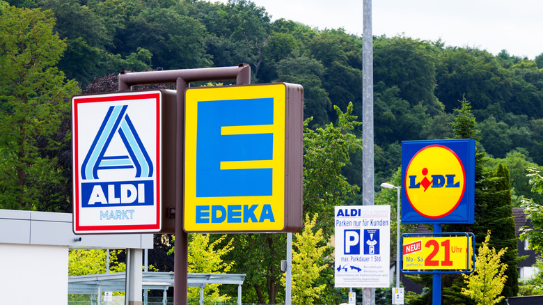 Signs for Aldi, Edeka, and Lidl against shrubbery background in Germany