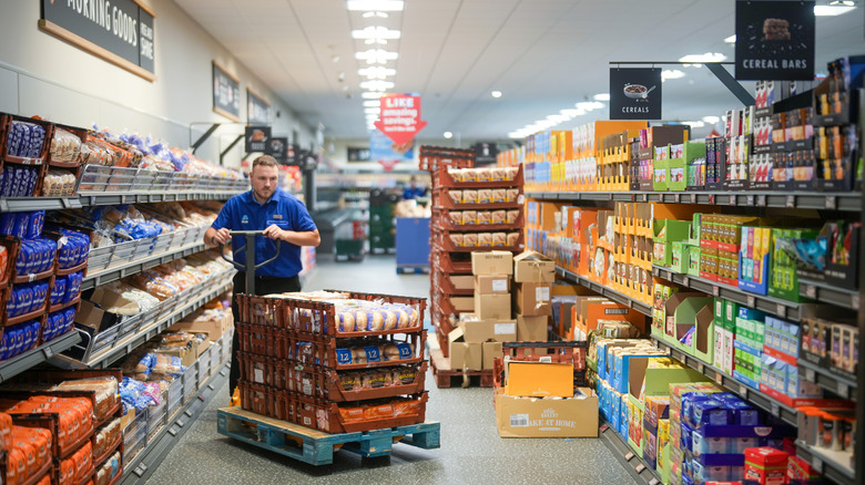 Man wheels pallets on a cart to restock shelves in Aldi