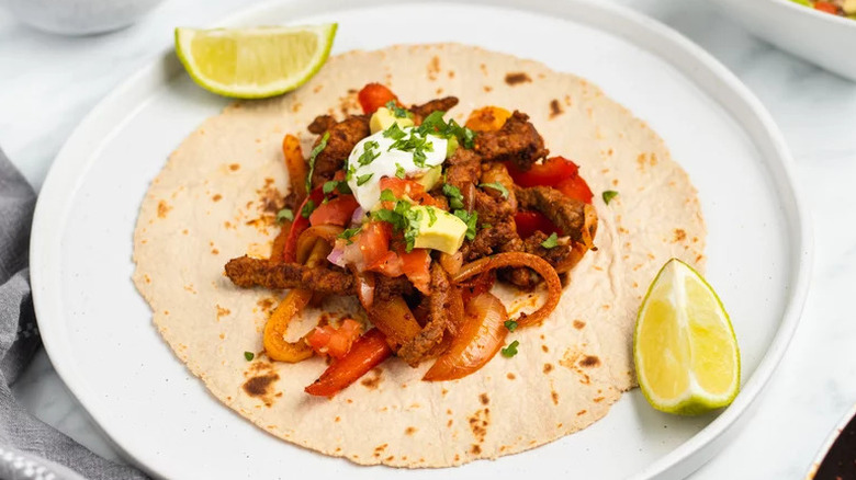 Sizzling Steak Fajitas on tortilla with lime wedges