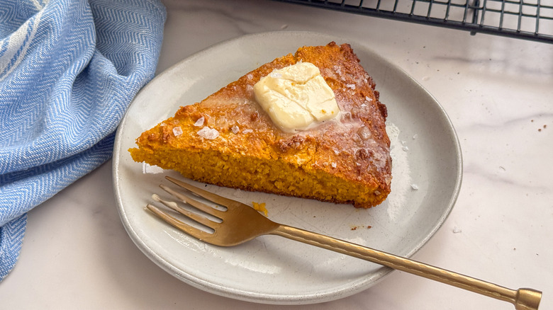 Slice of pumpkin cornbread topped with slice of butter on white plate with fork.