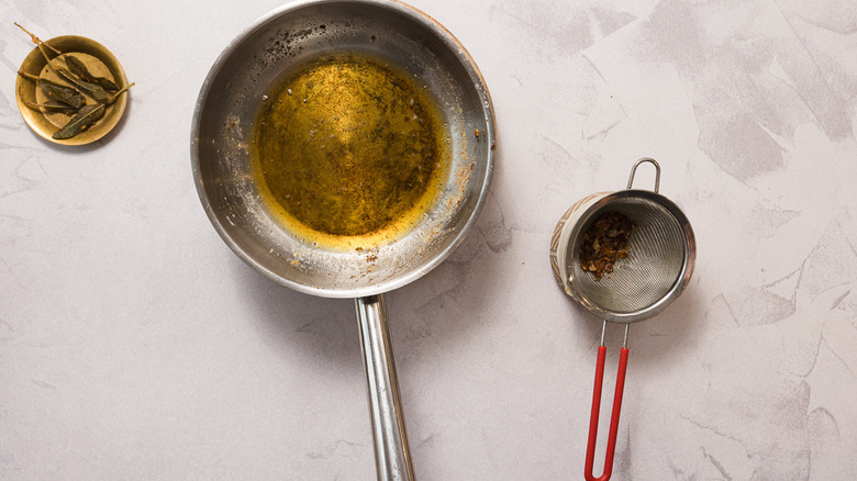 Drained brown butter in pan beside colander and fried sage