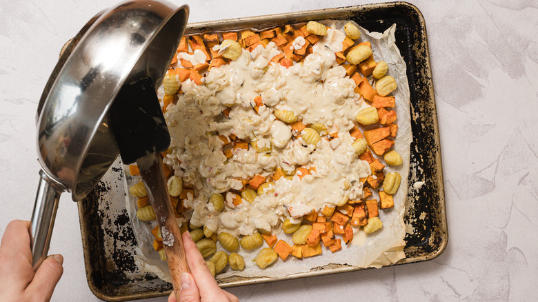 Pouring sauce over sheet pan with roasted butternut squash and gnocchi