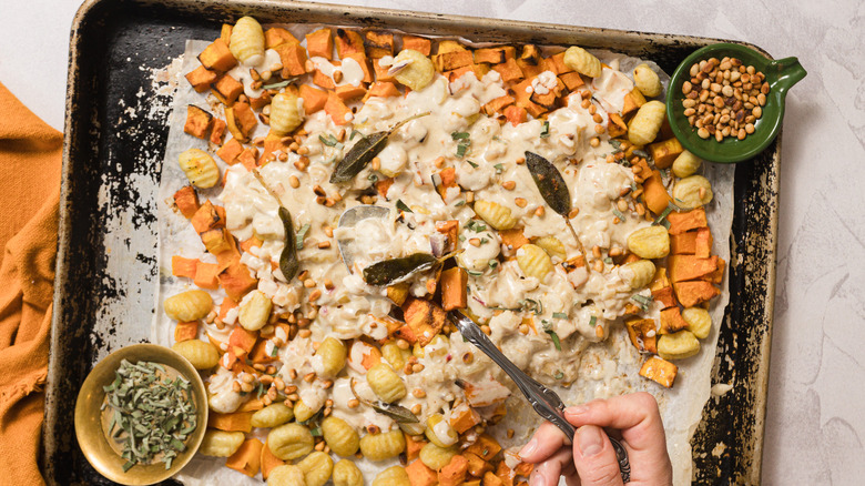 Holding a spoon over a sheet pan with gnocchi and butternut squash bake