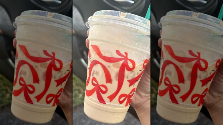 A person holding a Starbucks Iced Eggnog Latte in a holiday cup with red bows