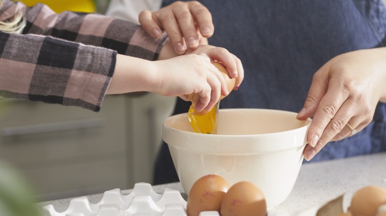 An adult helping a child crack eggs into a bowl