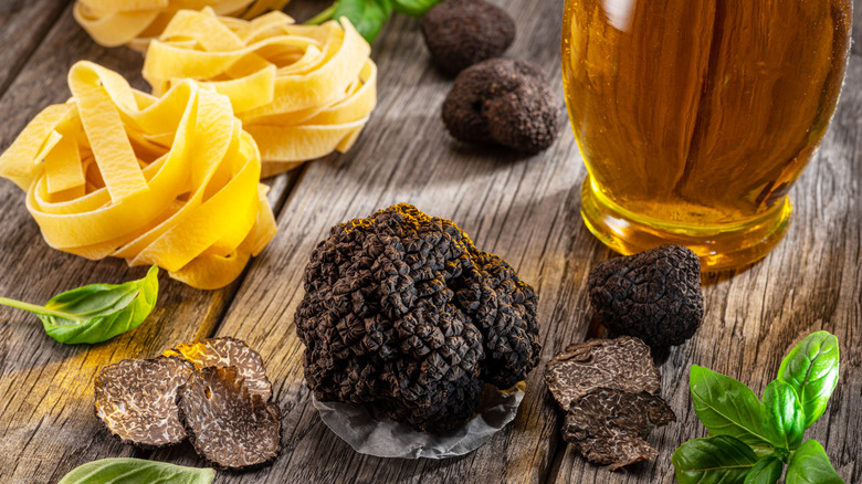 A large black truffle next to pasta and a glass of beer on a table