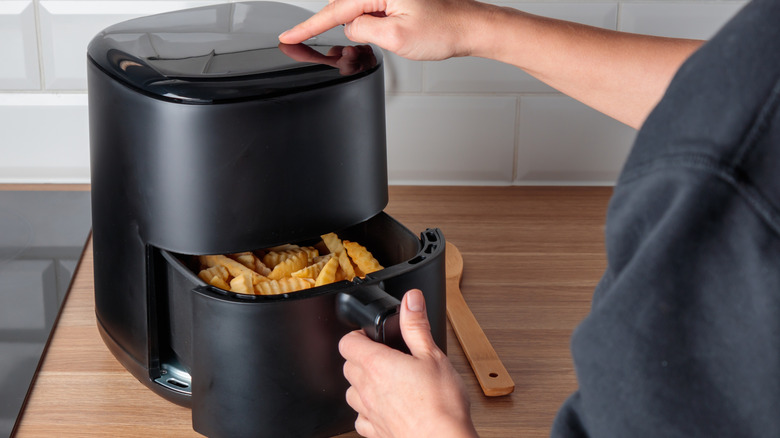 A close-up of a woman cooking fries in air fryer on kitchen worktop