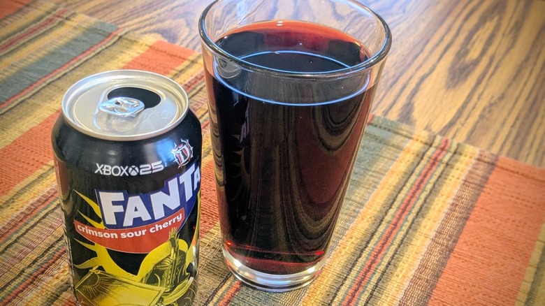 An open can of Fanta's Crimson Sour Cherry next to red soda in a glass