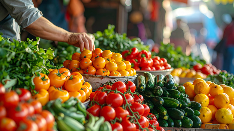 a hand reaching to pick up a tomato from a large farmstand display