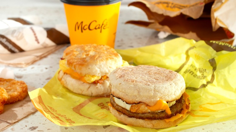 Two breakfast sandwiches from McDonald's on yellow paper wrapping next to yellow coffee cup with McCafe logo
