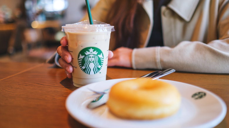 Person holding Starbucks drink cup with logo next to bagel on white plate