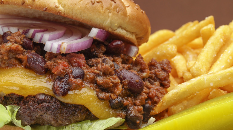 Chili cheeseburger with lettuce and red onion on a sesame seed bun with fries