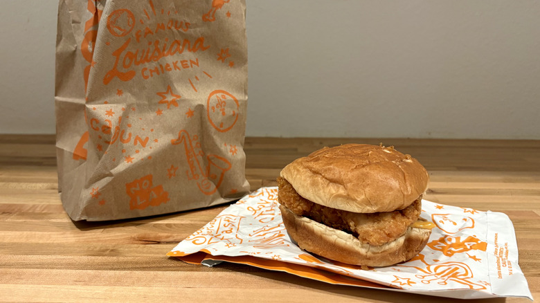 Popeyes sandwich with a big piece of fried chicken next to its bag