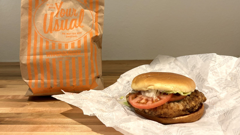 Whataburger chicken sandwich with tomato on top of its paper wrapper