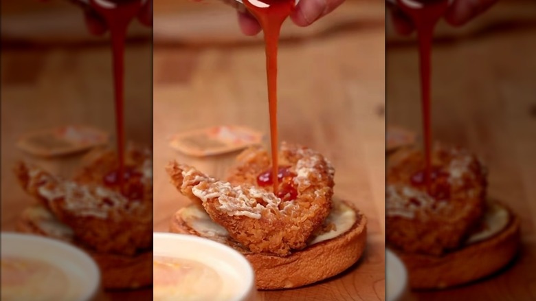 Pouring spicy sauce on an opened crispy chicken sandwich