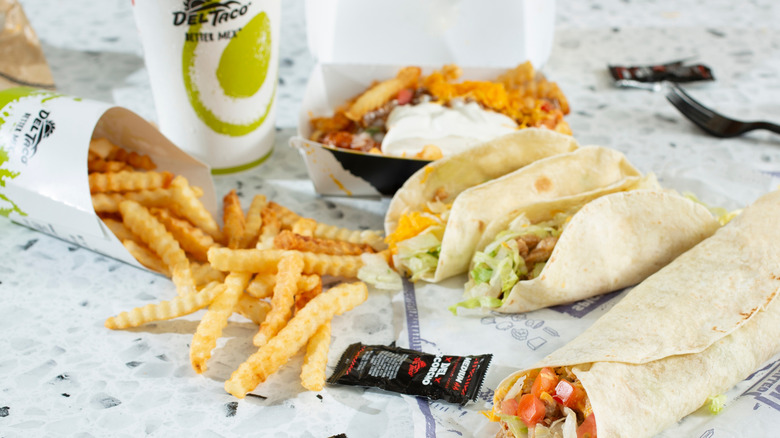 Various menu items from Del Taco displayed on a table among sauce packets and a drink cup