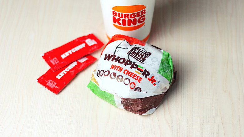 A Whopper Jr. with ketchup packets and a drink on a table