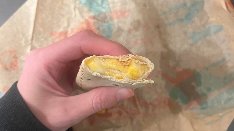 Close of hand holding Cheesy Roll Up over open packaging