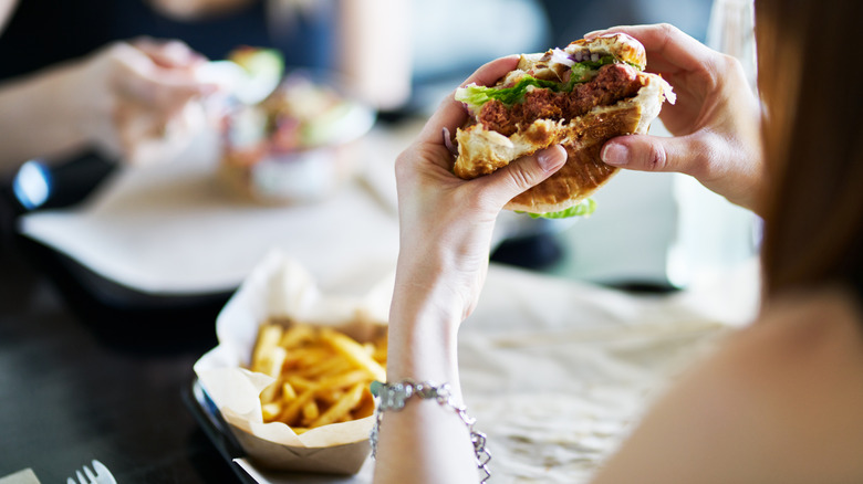 Over-the-shoulder photo of unidetified person eating a burger with fries on the table