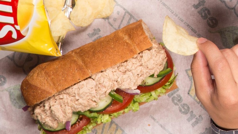 Subway tuna sub on paper with Lay's bag and hand holding chip