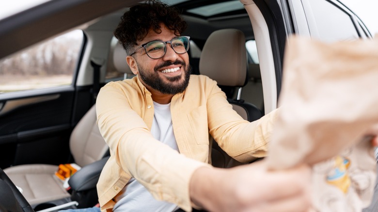 Man smiling in his car while receiving a bagged fast food order in the drive-thru