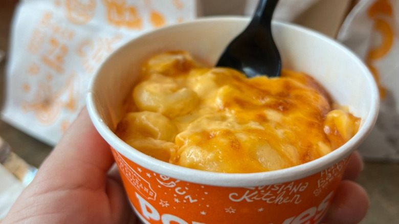 Hand holding a tub of Popeyes homestyle mac and cheese
