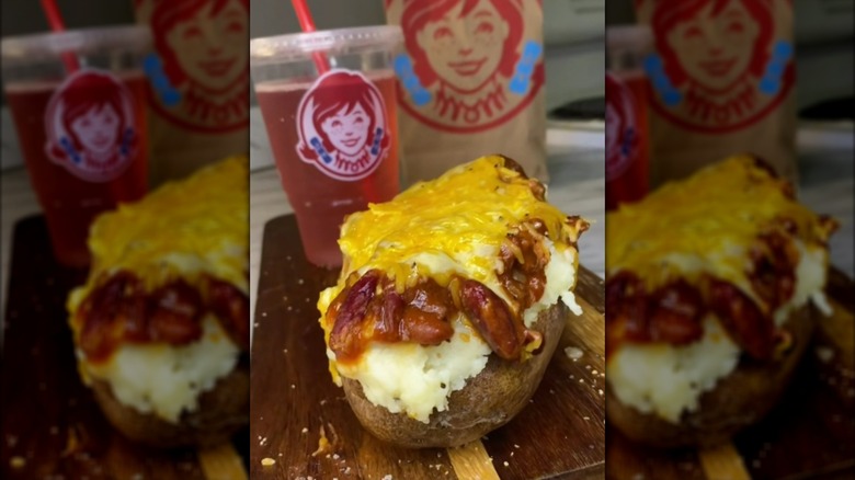 Wendy's chili cheese baked potato on a wooden board with a pink drink in a branded cup