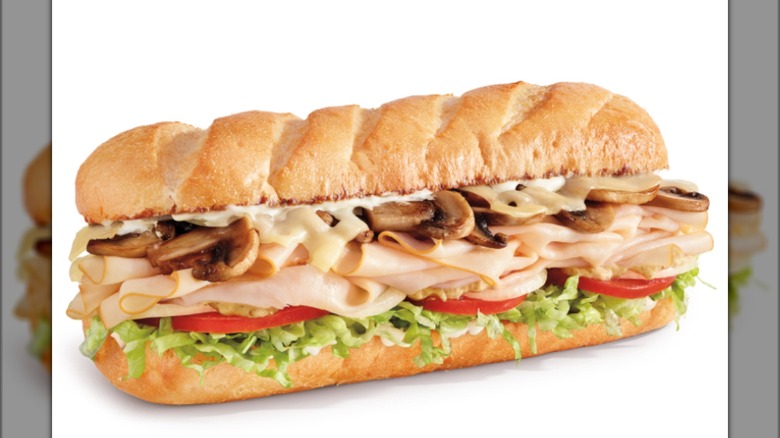Sub sandwich filled with sliced turkey, melted cheese, mushrooms, lettuce, and tomatoes