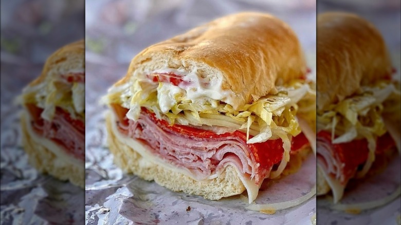 Halved sub sandwich with cured meats, lettuce, tomato, and mayo
