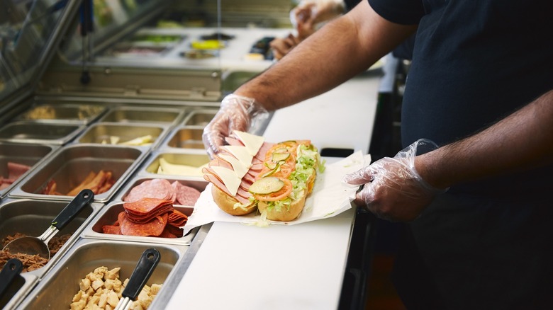 Sub restaurant employee making a protein-packed sandwich with meat, cheese, and veggies