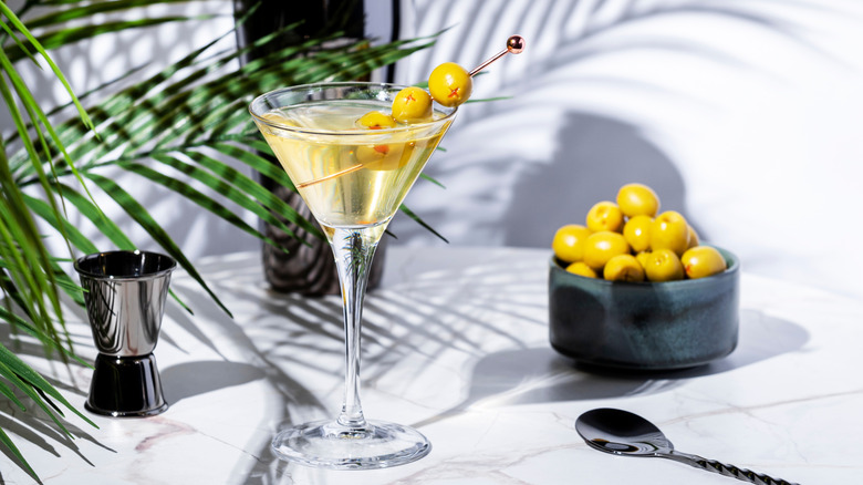 martini glass with olive skewer, beside it a jar of olives