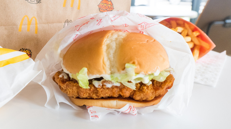 a McDonald's McCrispy sandwich sits halfway unwrapped with french fries and a paper bag in the background.